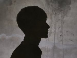 Artistic silhouette portrait of a person in profile, captured against a textured wall.